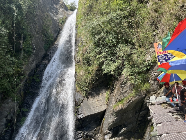 Group of people near a waterfall with umbrellas.