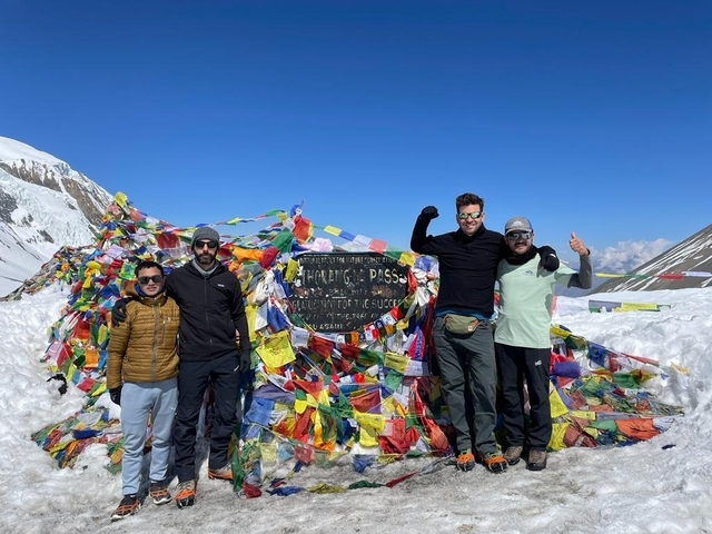 Group of trekkers celebrating at the Thorong La Pass with colorful prayer flags and snow.