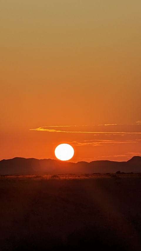 Sunset over a mountain range with an orange sky.