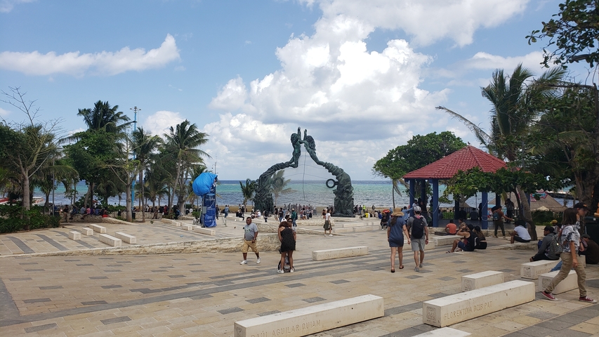 Coastal park with a large sculpture and people walking around.