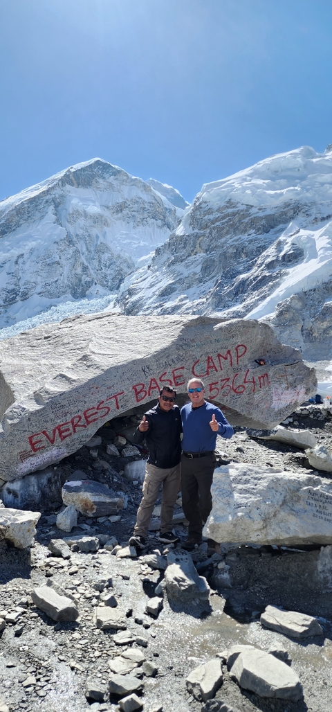       Two men standing in front of a large rock with Everest Base Camp sign.
  