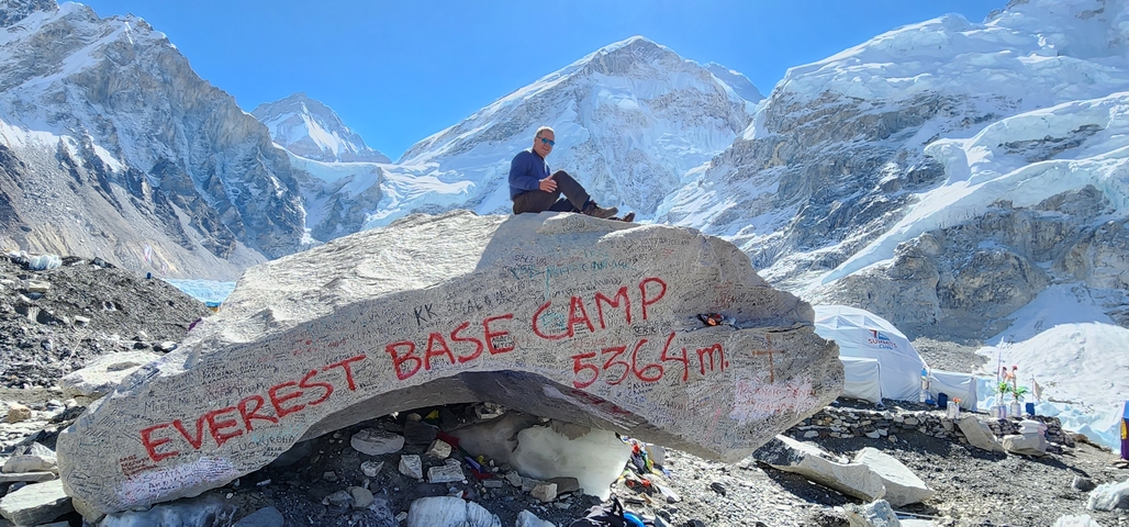       Man sitting on a rock at Everest Base Camp with mountains around.
  