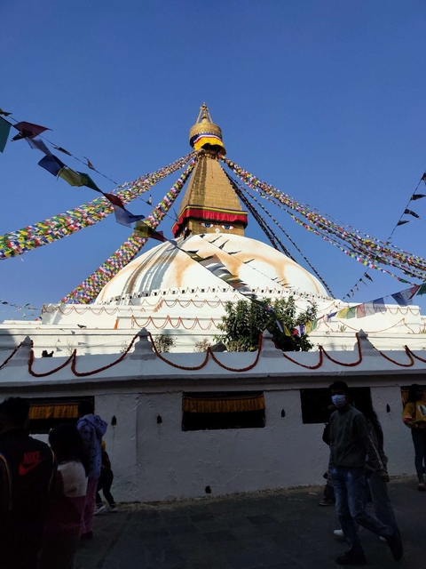 A stupa with prayer flags and people walking.
