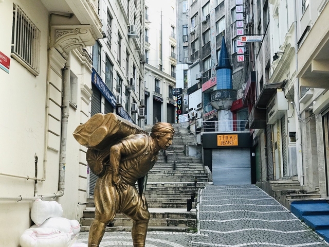 Golden statue on a steep street with storefronts.
