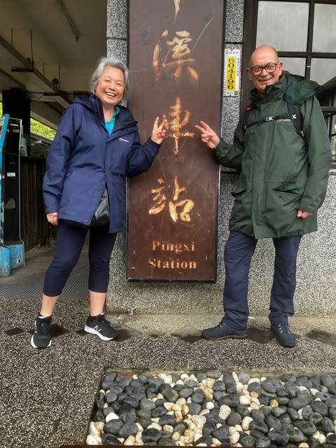 Two people posing with peace signs next to a sign at a station.