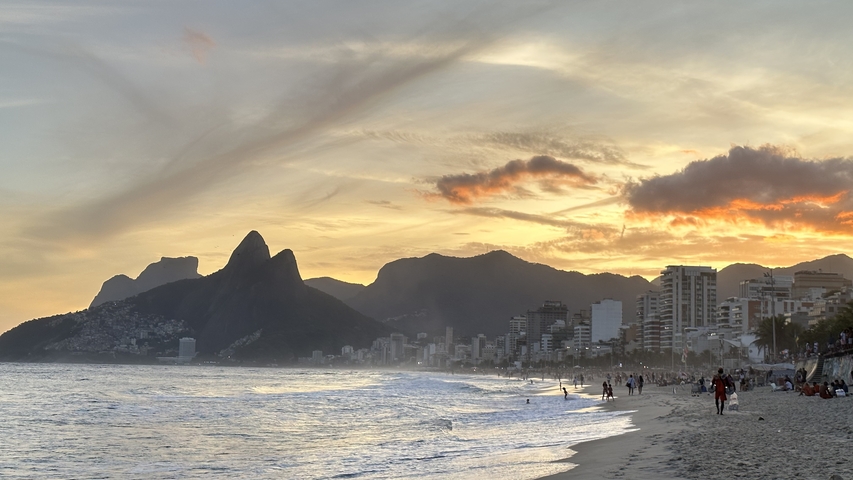 Beach at sunset with mountains and people in the water.