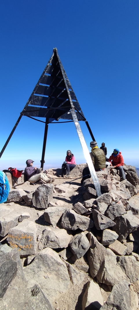       Group of hikers around a mountain summit marker.
  