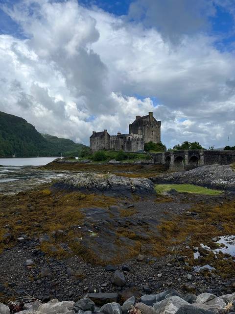 Castle by a rocky shore with cloudy skies.