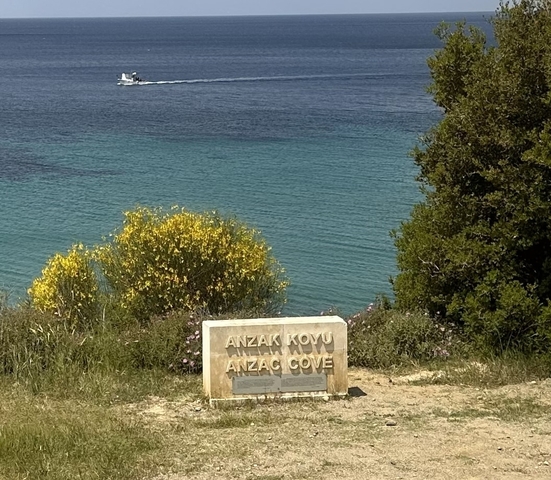       A coastline with clear blue water and a sign for Anzac Cove.
  