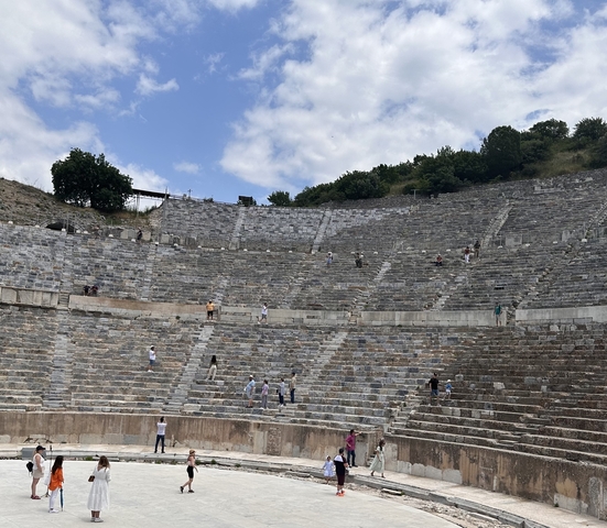       An ancient amphitheater with scattered visitors exploring.
  