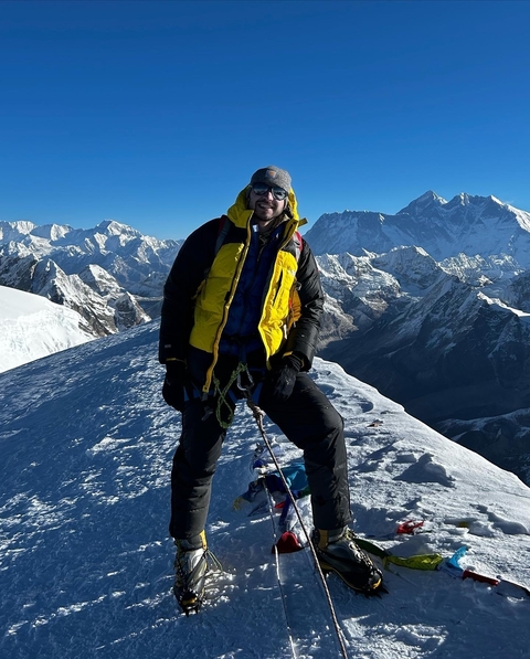 Man posing on a snowy mountaintop with mountains behind.