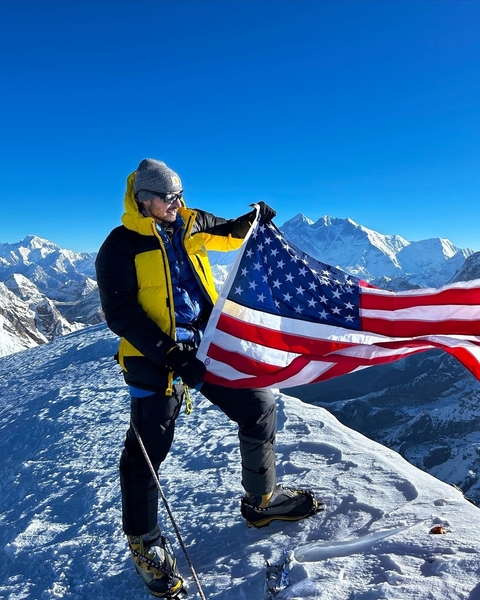 Man holding an American flag atop a snowy mountain.