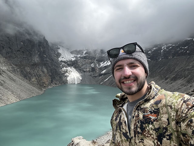 Man taking a selfie with a scenic mountain lake.
