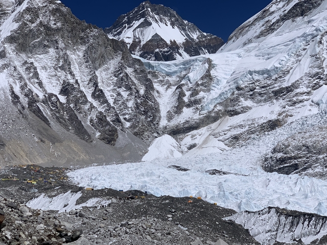 A glacier with surrounding rocky mountains under a clear sky.