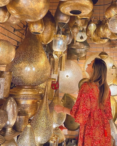 Woman admiring ornate brass lamps in a shop.