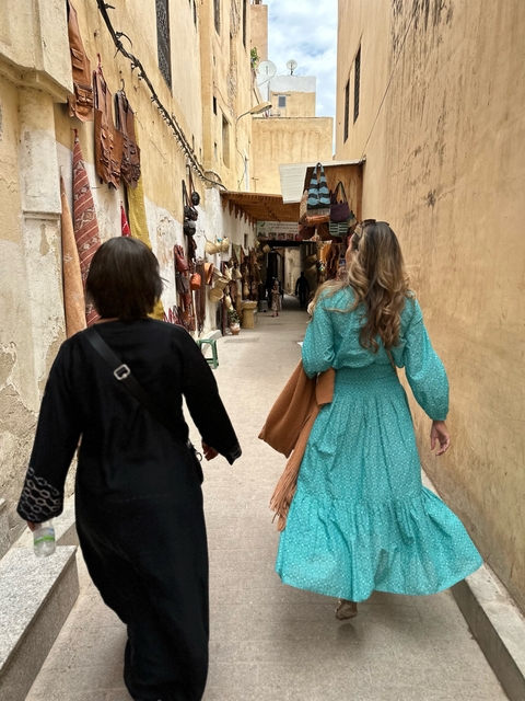 Women walking through a narrow alleyway lined with shops.