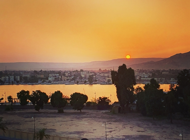 Sunset view over a river with a cityscape and trees.
