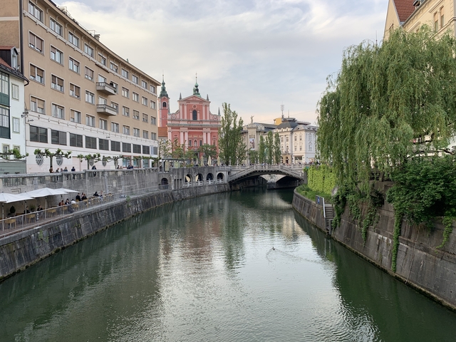      People walking along a canal with colorful buildings and a bridge.
  