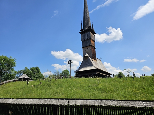 Wooden church with a tall spire on a grassy hill.
