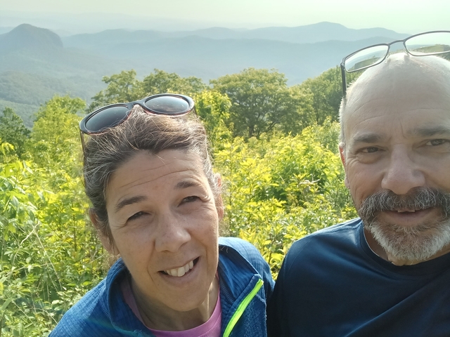 Close-up of two people smiling with a green landscape in the background.