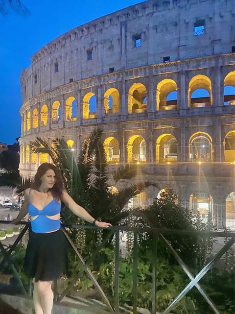 A woman posing in front of the Colosseum at night.
