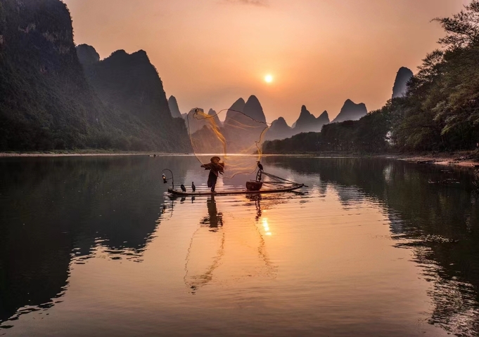 A fisherman casting a net at sunset in Yangshuo.