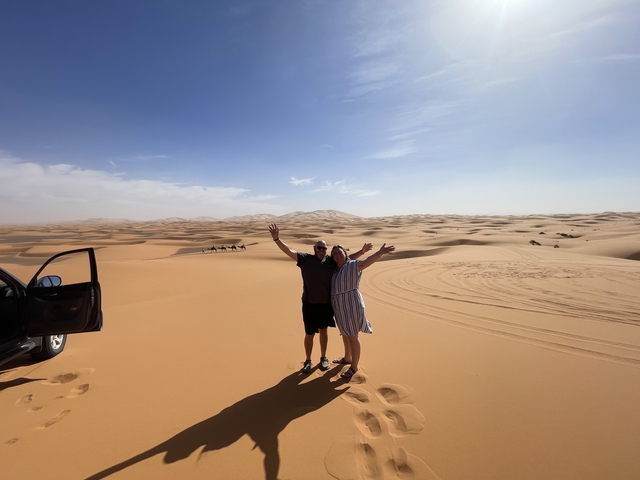       Two people standing in a vast desert landscape with dunes.
  