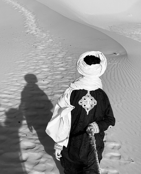       Person in traditional attire walking on sand dunes.
  