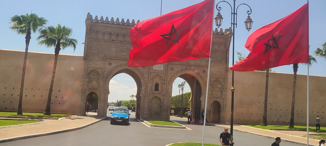       Gate with Moroccan flags and historical architecture.
  
