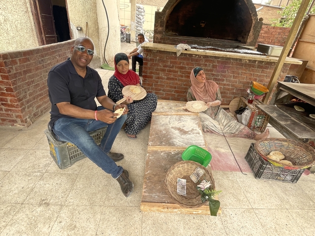A group of people making traditional bread in an outdoor setting with a brick oven.