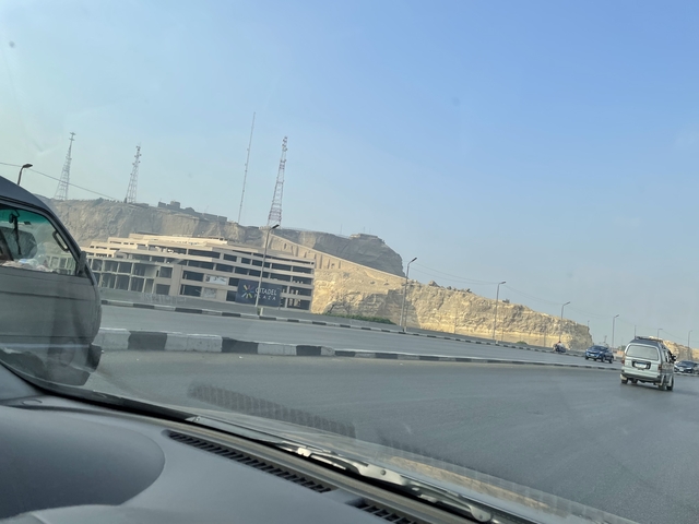 Highway view from inside a car with buildings in the distance.