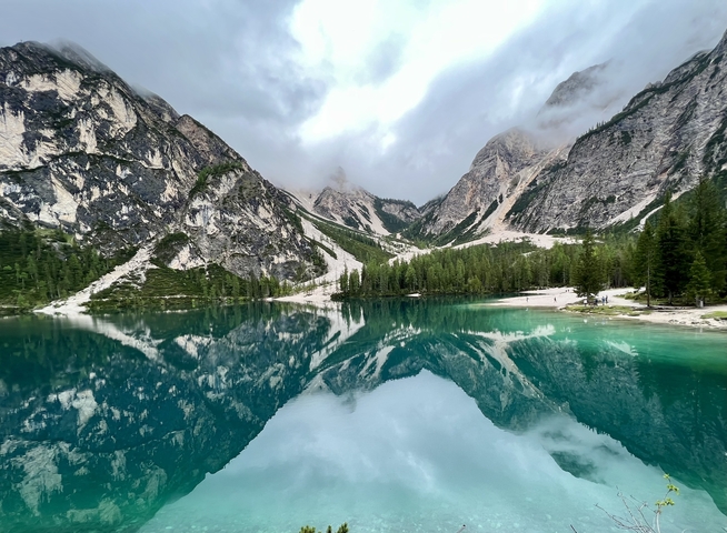 A stunning lake reflecting the surrounding mountains and trees under cloudy skies.