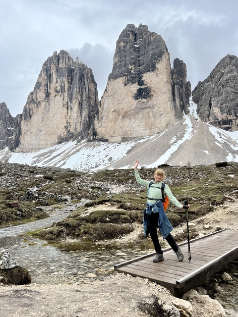 A person raising a hand in front of snowy and rocky mountain peaks.