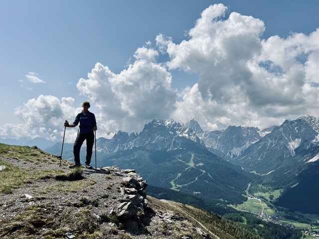 A hiker standing on a hill with a panoramic view of mountains and clouds.