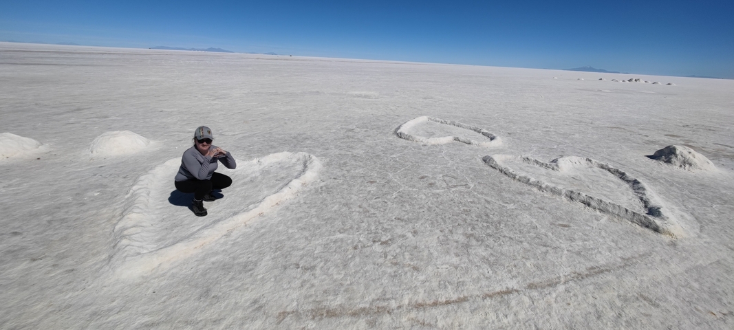 Person near a carved heart shape on a salt flat.