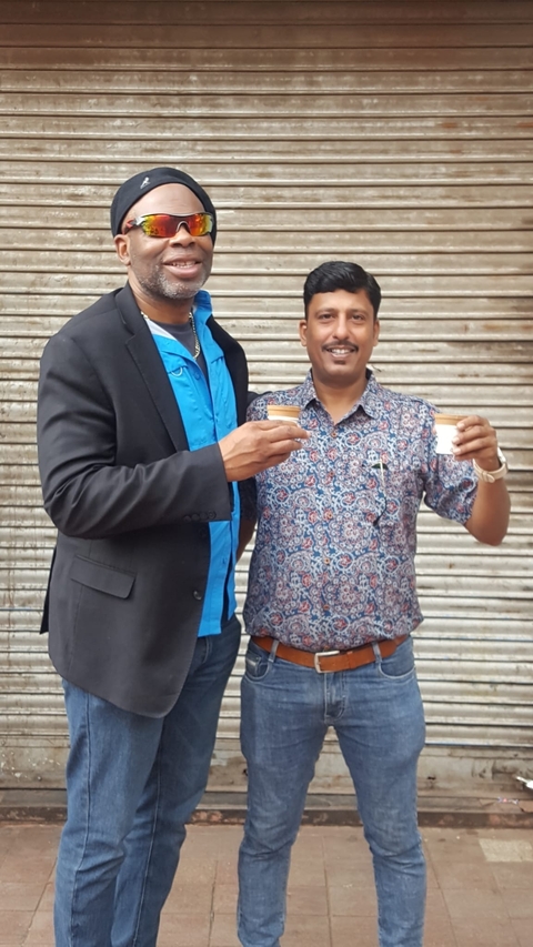 Two people holding small cups, standing in front of a metal shutter.