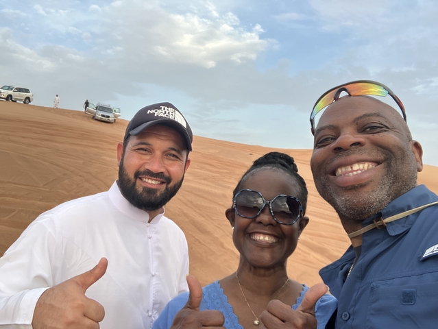 Group selfie in a desert setting with cars in the background.