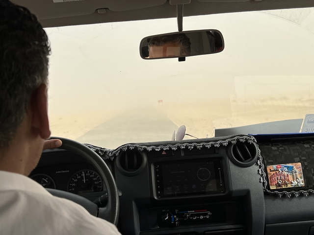 View from inside a vehicle during a sandstorm with person driving.