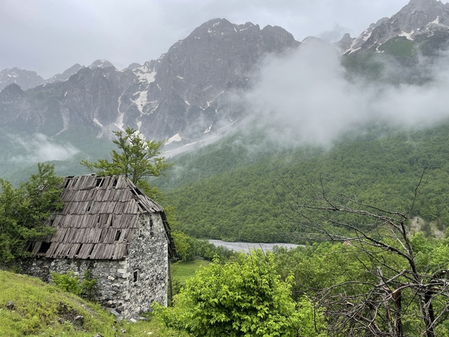 Old stone cabin in front of misty mountains.