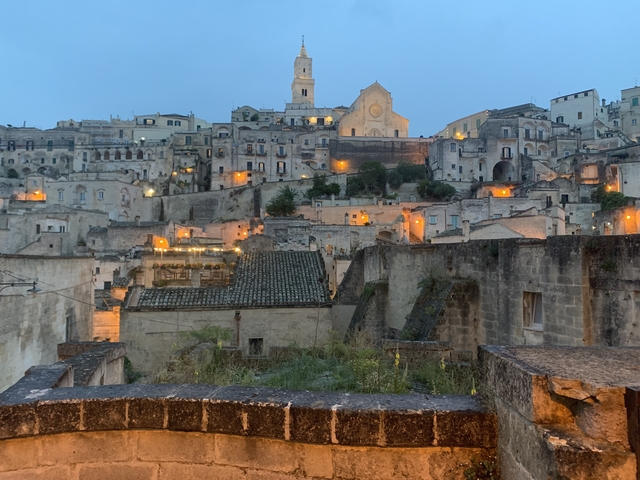       Cityscape of Matera with illuminated buildings at dusk.
  