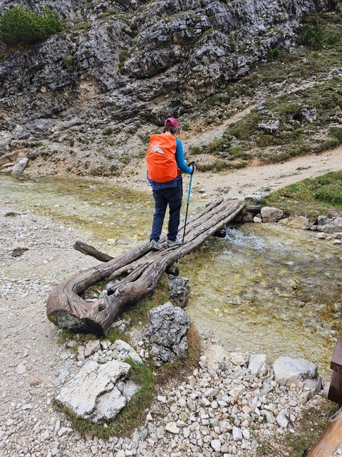 A hiker crossing a stream on a wooden bridge.