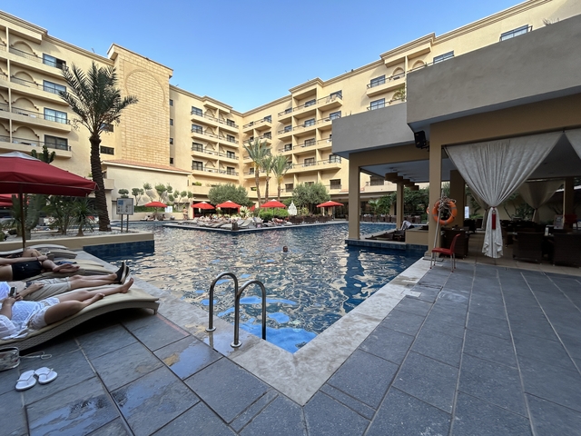 Hotel poolside with people relaxing under umbrellas.