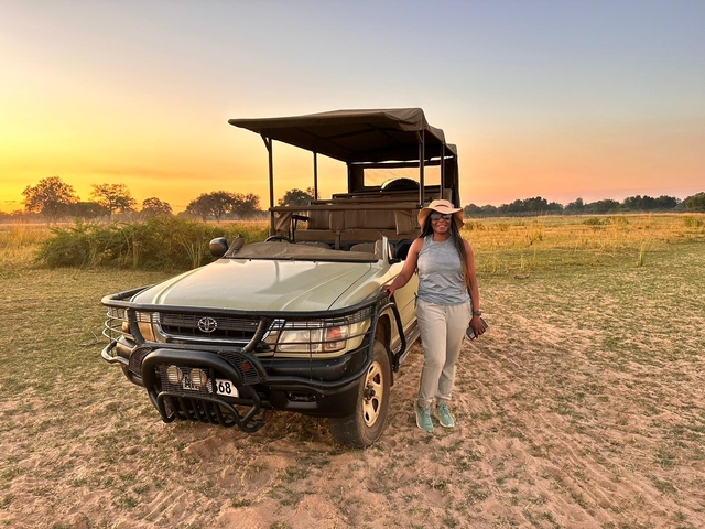 Person standing beside a safari vehicle at sunset.