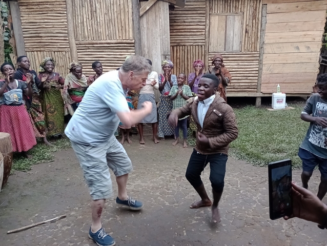 People engaged in a cultural dance performance in front of a wooden structure.