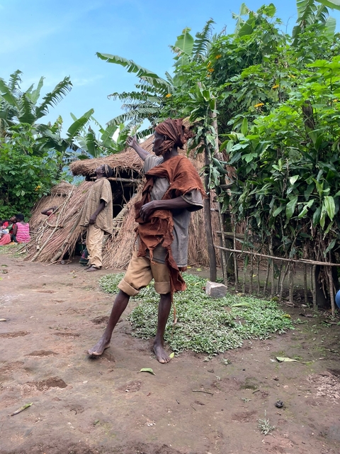 Person in traditional clothing beside a thatched structure.
