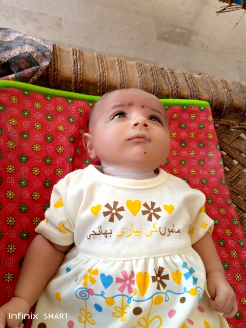       Baby lying on a patterned blanket looking upwards.
  