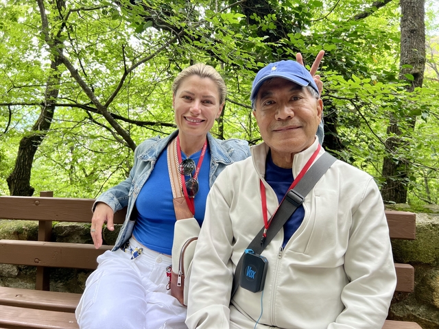 Two people sitting on a bench in a forest setting.
