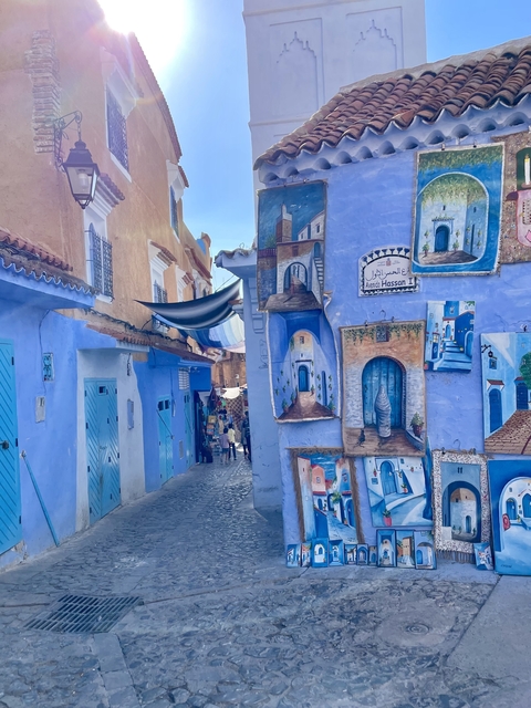       Bright blue alley with artwork and market in distance
  