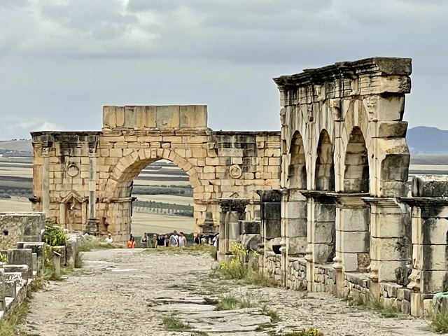       Ancient Roman ruins with an archway and tourists
  