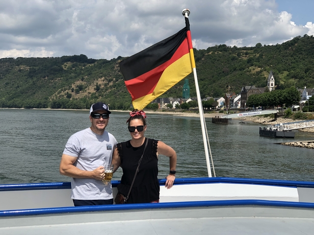 Couple posing on a boat with a German flag and scenic background.